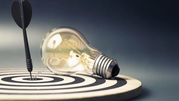A light bulb lying on a target with a dart stuck in it.  