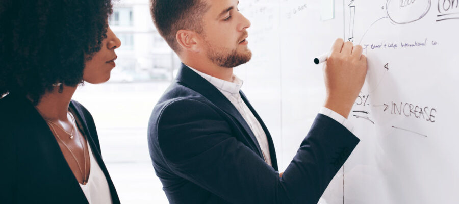 Ein Mann und eine Frau stehen vor einer Wandtafel. Beide sind von einer Finanzfirma  und erarbeiten gemeinsam eine Rechnung.