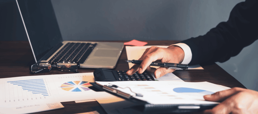 Chun Analysis Cover image - Person working at a desk with a calculator, laptop, and financial documents. Diagrams and tables can be seen on the papers.