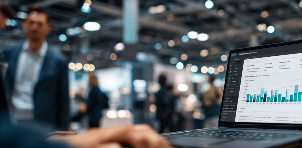 Fachleute in smarter Business-Kleidung arbeiten gemeinsam an einem hellen Arbeitsplatz. Auf dem Laptop-Bildschirm ist etwas verschwommen ein dynamisches Planungs-Dashboard mit vergleichenden Prognosen und modularen Planungsansichten zu sehen. Der Hintergrund zeigt hohe Decken, was auf einen Verkaufsladen hindeutet, der elektronische Waren beinhaltet.